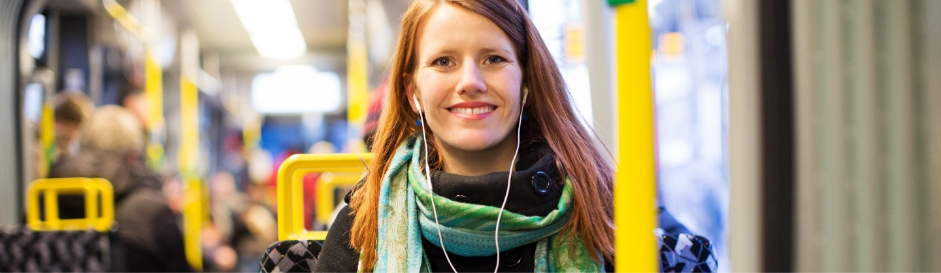 Eine junge Frau sitzt im Bus, hört Musik und lächelt