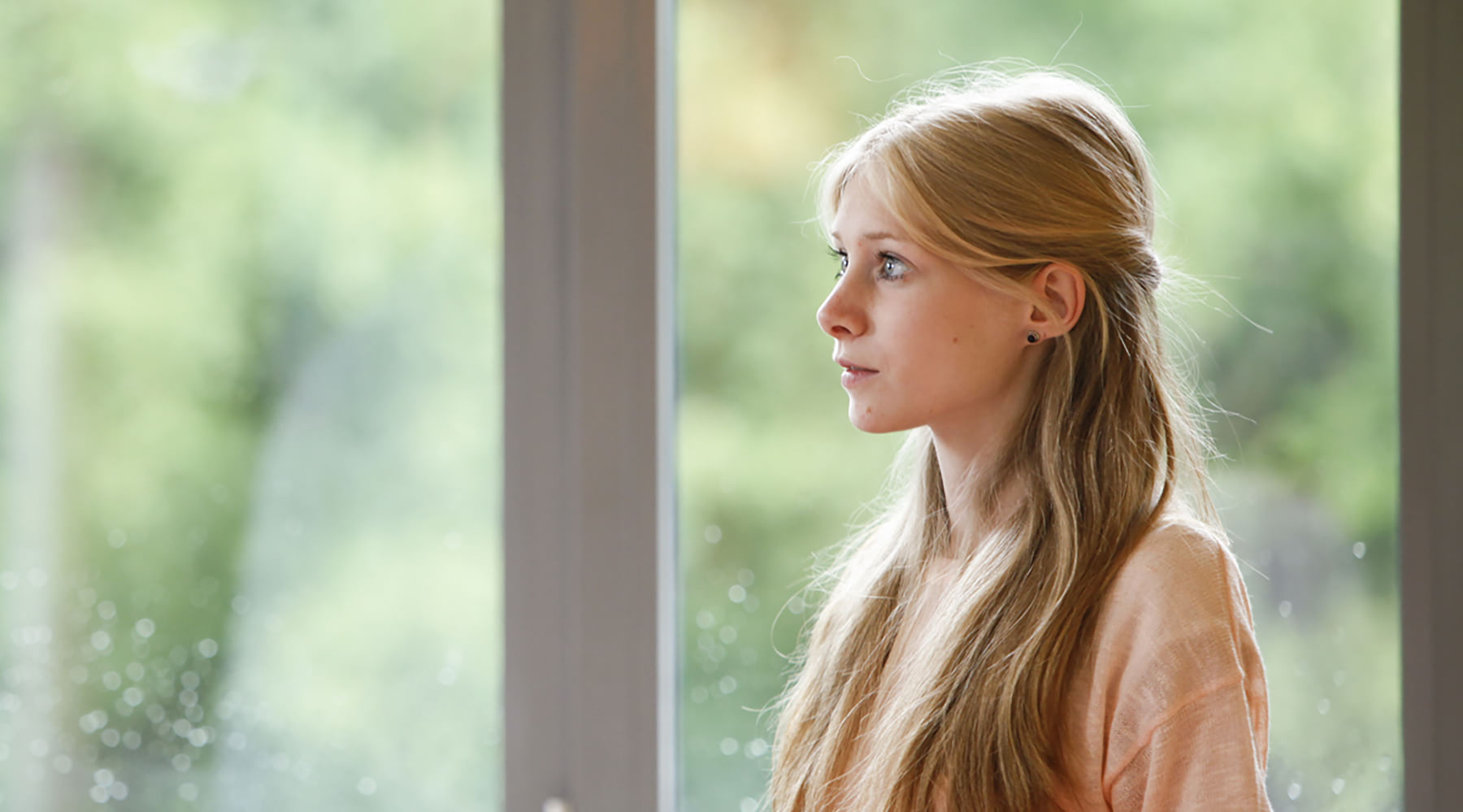 Eine junge Frau steht vor einem großen Fenster und schaut zur Seite