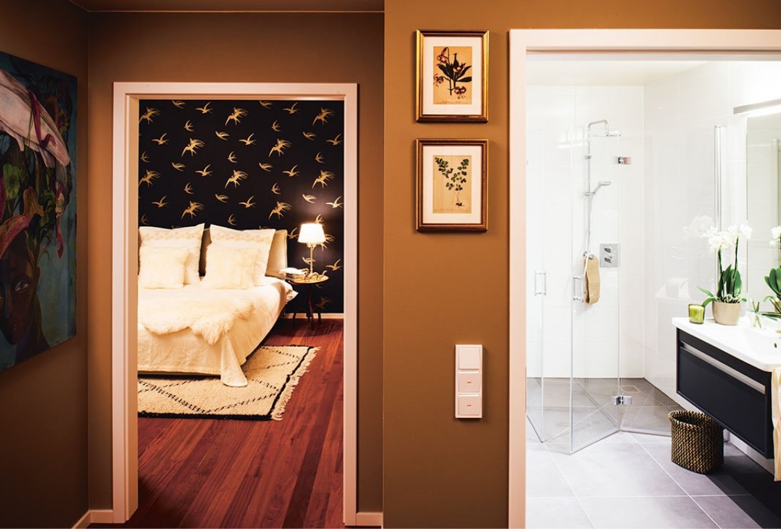 Blick aus dem Flur in ein stilvoll eingerichtetes Schlafzimmer auf der linken Bildhälfte und einem freundlich-hellem Badezimmer auf der rechten Seite