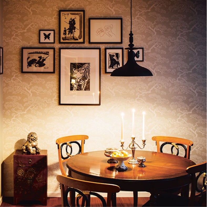 Blick auf einen kleinen runden Esstisch mit einer gemusterten Tapete und Bilderrahmen an der Wand